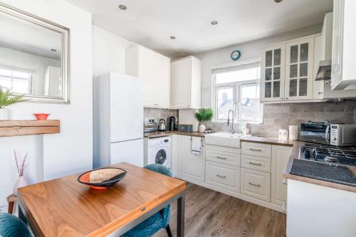 a kitchen with white cabinets and a wooden table at Chic and Cheerful Flat in Willesden Green in London
