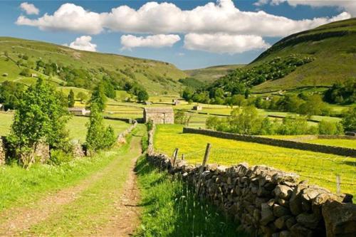 a dirt road in a field next to a stone wall at Fern Hse Grassington; central yet quiet & parking in Grassington