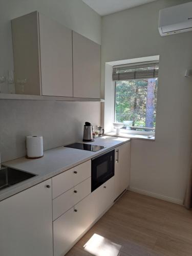 a kitchen with white cabinets and a sink and a window at Kurortas Apartments in Palanga