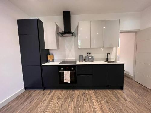 a kitchen with black and white cabinets and a wooden floor at Star London Finchley Road 1-Bed Sanctuary in London