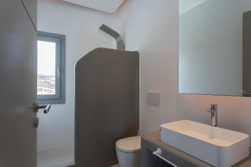 Un baño con lavabo, inodoro y espejo. en Villa Indigo - Mykonos, en Mykonos ciudad