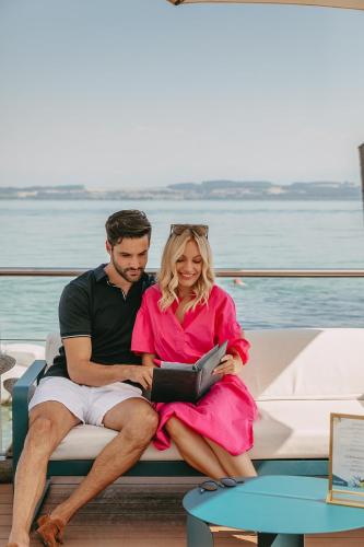a man and woman sitting on a bench on a boat at Hotel Palafitte in Neuchâtel