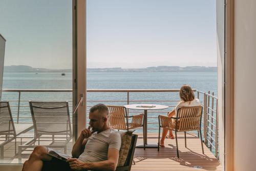a man sitting on a balcony talking on a cell phone at Hotel Palafitte in Neuchâtel