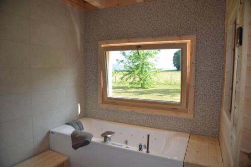 La salle de bains est pourvue d'une baignoire et d'une fenêtre. dans l'établissement chalet bien-être 100m² -Gîte les 4 saisons - Lac de Chalain, à Marigny