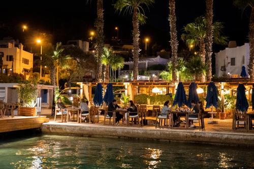 a group of people sitting at tables by the water at night at Torbahan Hotel in Torba