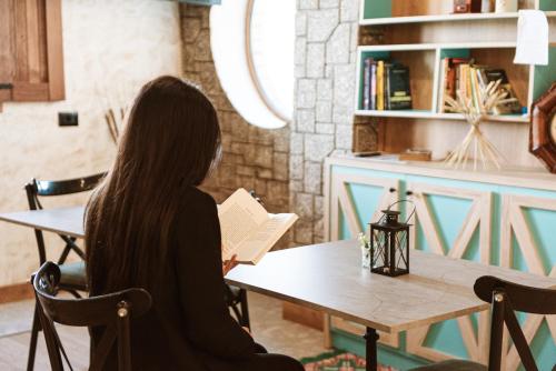 a woman sitting at a table reading a book at Hotel Taverna Devolli in Kuçovë