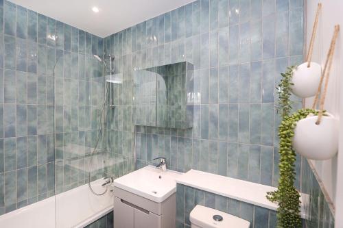 a blue tiled bathroom with a sink and a toilet at Luxury interior designed 1 bed in London