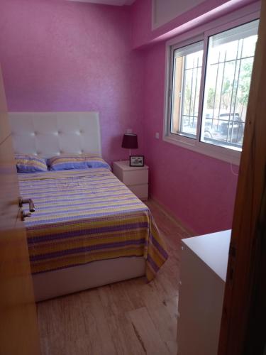 1 dormitorio con 1 cama con paredes de color púrpura y ventana en Résidence Al Jazera, en Les Camps