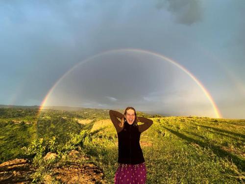 a woman standing in a field with a rainbow in the background at Sipi Backpackers in Kapchorwa