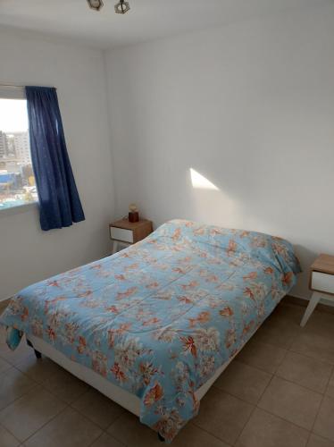 a bedroom with a bed with a blue comforter and a window at Vistas Meseta Patagónica II in Trelew