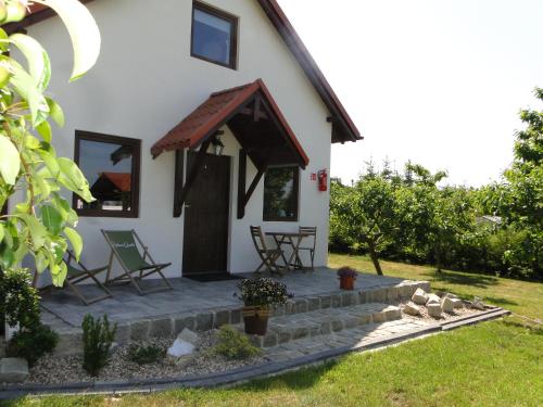 a small white house with a porch and two chairs at Domki Zielona Osada in Szczenurze