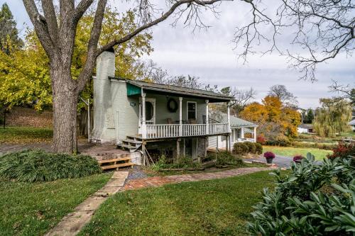 una casa antigua con un porche y un árbol en By the Side of the Road Inn & Cottages, en Harrisonburg