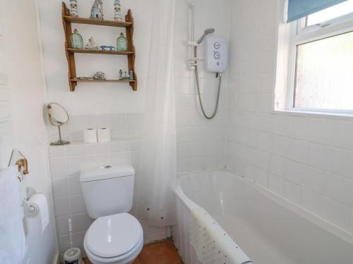 a white bathroom with a toilet and a bath tub at Studland Cottage in Swanage