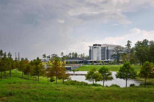 a park with a building and a river and trees at Houston CityPlace Marriott at Springwoods Village in The Woodlands