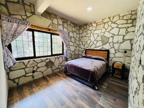 1 dormitorio con pared de piedra, cama y ventanas en Finca Bermúdez - Cabaña del Rio, en Huasca de Ocampo