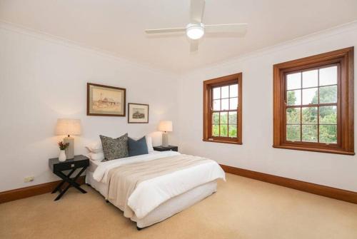 Un dormitorio blanco con una cama y dos ventanas. en Hahndorf Luxury Retreat 5 bedrooms for 12 guests, en Hahndorf