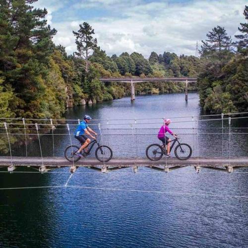two people riding bikes on a bridge over water at Black Beauty - Spacious Family Retreat for 12 with Spa in Mangakino