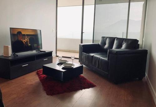 a living room with a black couch and a tv at Las Condes, al lado de Marriott y Parque Arauco, ideal para Trabajo, Salud y Vacaciones in Santiago