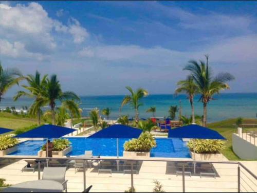 una piscina con sombrillas azules y el océano en Lujoso y Familiar Apartamento de Playa y Golf en San Carlos Panamá en San Carlos