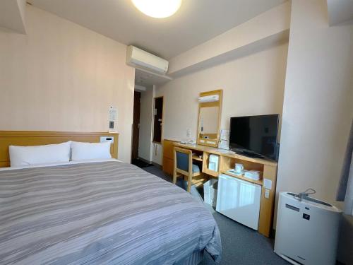 um quarto de hotel com uma cama e uma secretária com uma televisão em Hotel Route-Inn Aizuwakamatsu em Aizuwakamatsu