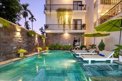 a pool with chairs and umbrellas next to a building at Tomorrow Oasis Boutique Villa Hoi An in Hoi An