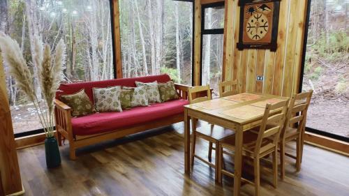 ein Wohnzimmer mit einem roten Sofa und einem Tisch in der Unterkunft Cabaña en Coñaripe Sector Termas Geométricas in Coñaripe