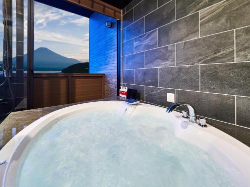 La salle de bains est pourvue d'une grande baignoire et d'une fenêtre. dans l'établissement Rakuten STAY VILLA Lake Yamanakako 101 View bath Mt Fuji View, à Yamanakako
