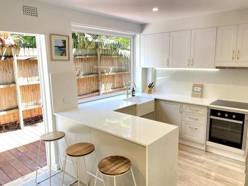 una cocina con armarios blancos y una barra con taburetes en Dee Why Town House, en Deewhy