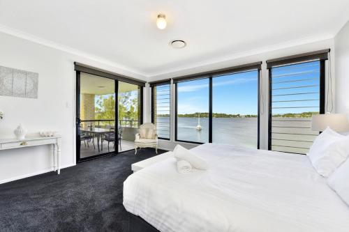 a bedroom with a white bed and a view of the water at Water's Edge Apartment 2 absolute waterfront at Fishing Point on Lake Macquarie in Fishing Point