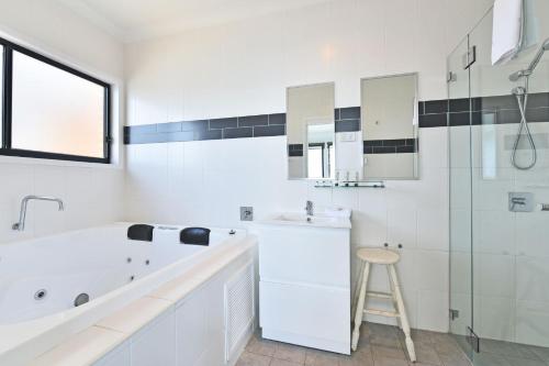 a white bathroom with a tub and a sink and a stool at Water's Edge Apartment 2 absolute waterfront at Fishing Point on Lake Macquarie in Fishing Point