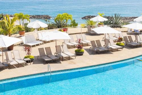 a pool with chairs and umbrellas next to the ocean at Marriott Venezuela Hotel Playa Grande in Playa Grande
