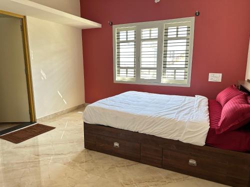een slaapkamer met een bed met rode muren en een raam bij Anthara Service Apartment in Belūr