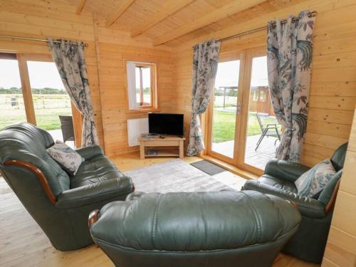 a living room with two leather couches and a television at Ty Mai, Parc Y Fronwen in Newborough