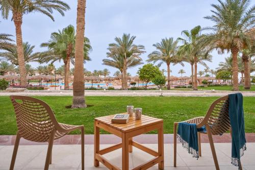 een tafel en twee stoelen met een tafel en palmbomen bij Three Corners Sea Beach Resort in Baai van Coraya