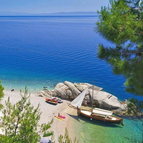 a boat on a beach with people on the shore at Apartments Chiara mit Meerblick und Pool und Jacuzzi in Lovran