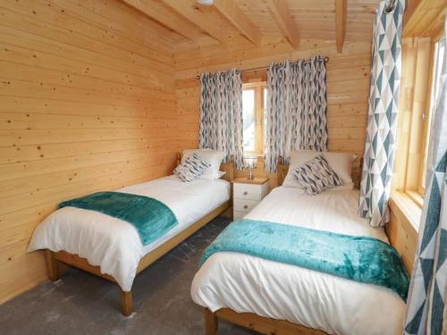 two beds in a room with wooden walls at Ty Presto, Parc Y Fronwen in Newborough