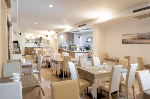 a restaurant with tables and white chairs and a counter at Hotel Kennedy in Lido di Jesolo