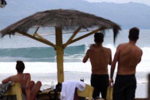 three men standing under an umbrella on the beach at Rumah Nalu surf camp in Krui
