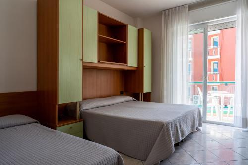 two beds in a hotel room with a window at Hotel Kennedy in Lido di Jesolo