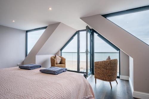 a bedroom with a bed and two chairs and windows at Beach View Breeze Family Holiday Home on the Shore in Pevensey