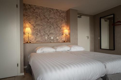 a bedroom with a large white bed with two lamps at Hof van Schoorl in Schoorldam