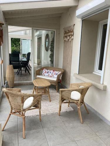 un patio avec des chaises en osier et un banc sur un porche dans l'établissement Gîte COQUELICOT F2 avec piscine et SPA, à Saint-Jean-de-Boiseau