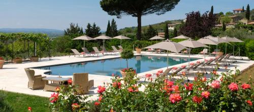 a swimming pool with chairs and umbrellas and flowers at Relais & Châteaux Il Falconiere in Cortona