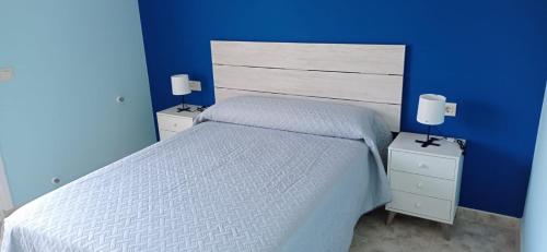 a blue bedroom with a white bed and two night stands at Apartamentos M° Esther in A Lanzada