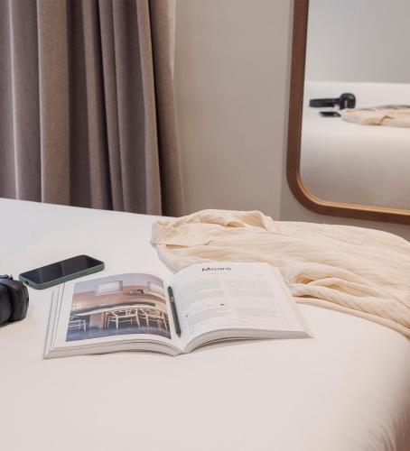 an open book on a bed with a cell phone at Room Mate Oliveira - City Centre, Valencia in Valencia