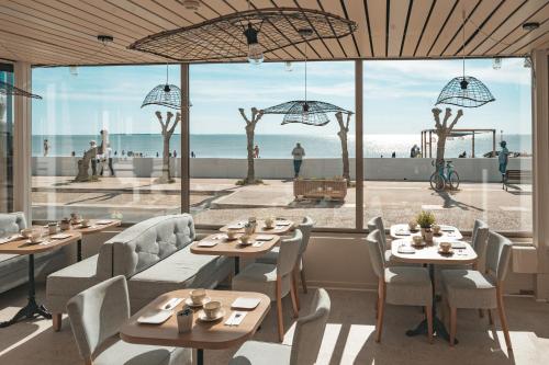 Un restaurante con mesas y sillas y vista a la playa. en Hôtel Le Rivage vue sur mer - Châtelaillon-plage, en Châtelaillon-Plage
