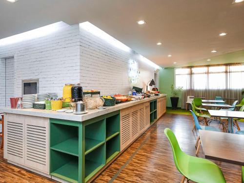 a kitchen with a counter with green chairs and tables at ibis Styles Araraquara in Araraquara