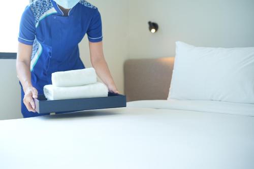 a woman standing next to a bed with a tray of towels at GO Hotel Si Racha at Central Si Racha in Si Racha