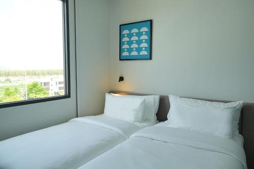 two white beds in a room with a window at GO Hotel Si Racha at Central Si Racha in Si Racha