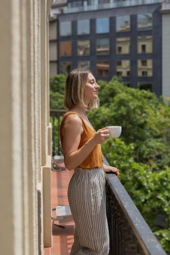 a woman standing on a balcony holding a cup of coffee at Gran Hotel Havana 4Sup by Escampa Hotels in Barcelona